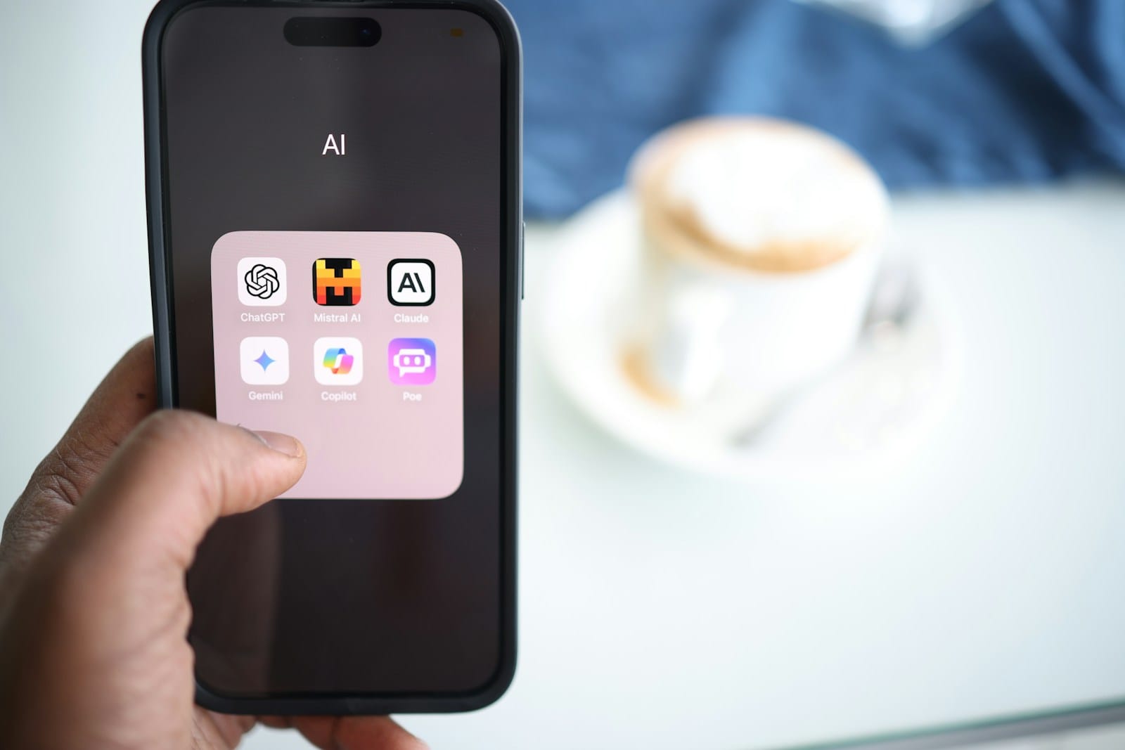 手に持ったスマートフォンに、AIのアプリが並んだフォルダが映っている