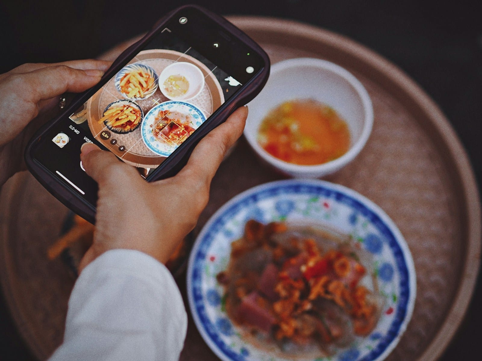 テーブルの料理を、スマートフォンで撮っている手元