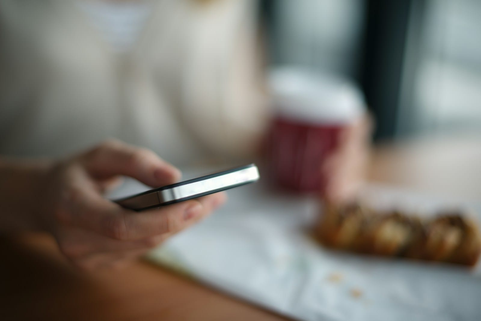 手に持ったスマートフォンを見ている、テーブルの手元